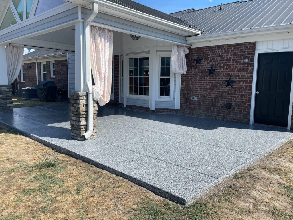 A brick house with a covered patio, featuring stone pillars, draped curtains, and star decorations on the wall under a blue sky.