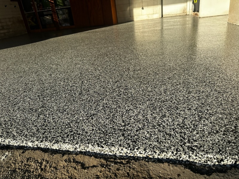 A smooth, newly finished concrete floor in a sunlit garage with partial view of a door and wall in the background.
