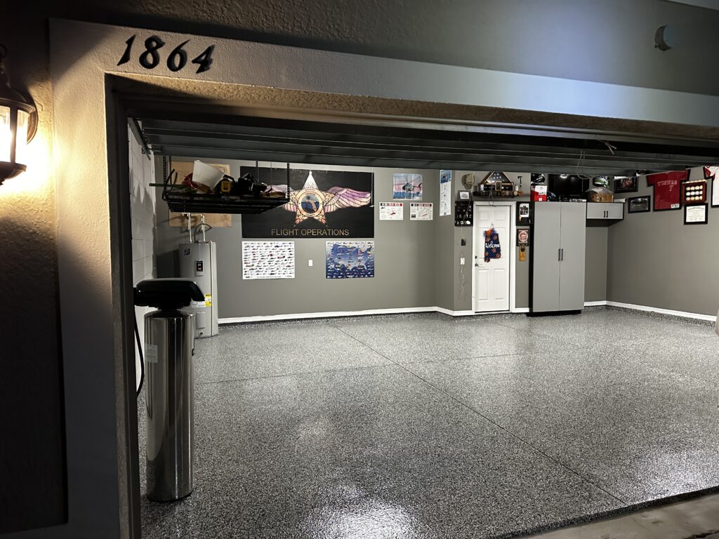 Clean, organized garage displaying aviation memorabilia, grey cabinets, and wall-mounted storage. Address "1864" above the open door, with a polished floor.
