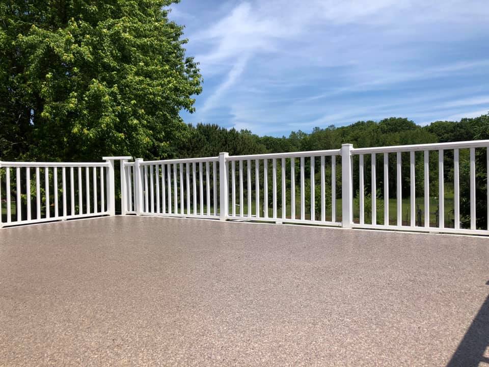 A large patio with white railings overlooks lush green trees under a clear blue sky on a sunny day.