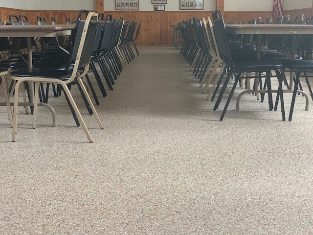 A room with rows of black chairs and tables. Wooden paneling and framed photos on walls. An American flag is visible.